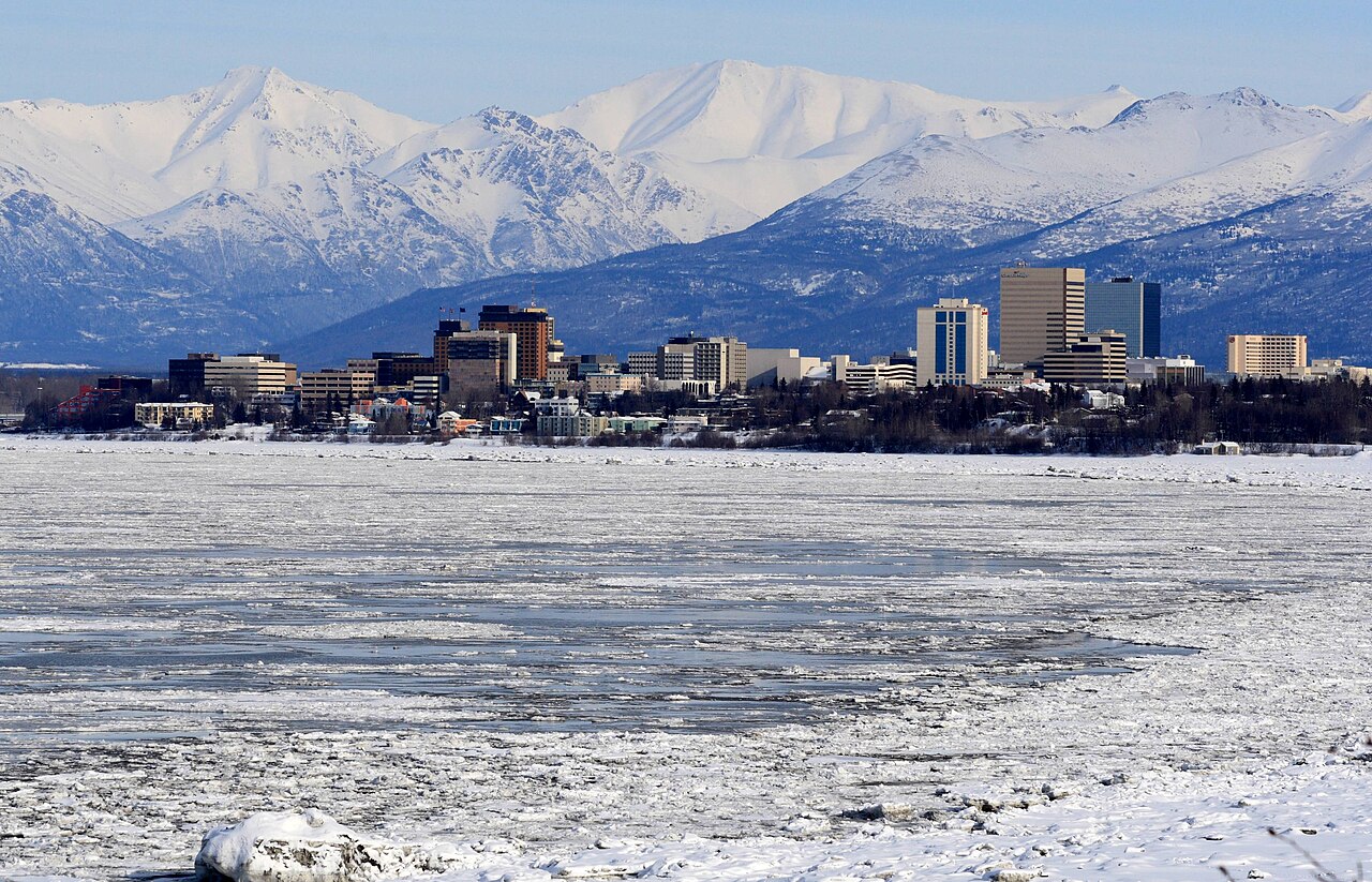 Immeubles du centre d’Anchorage devant des montagnes enneigées, avec de la glace au premier plan