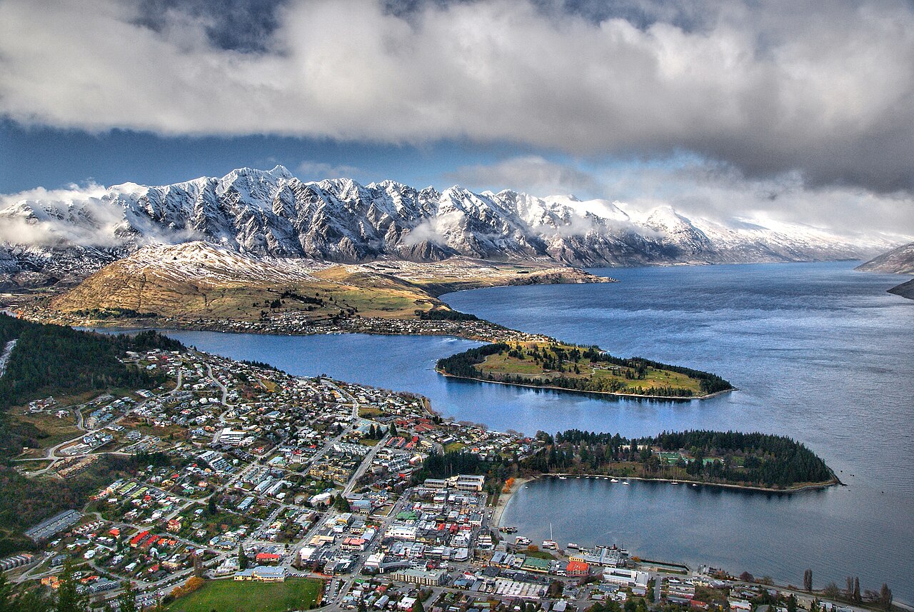 Vue aérienne de Queenstown au bord du lac Wakatipu, face à des montagnes enneigées.